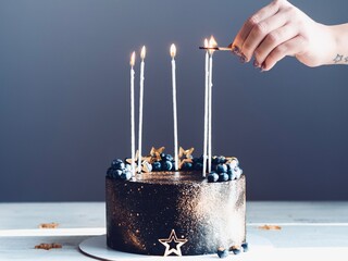 A girl lights candles on a cake with a match. Black and gold cake with candles
