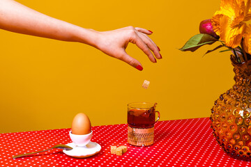 Served breakfast table. Food pop art photography. Tea, egg and flowers on red tablecloth over...