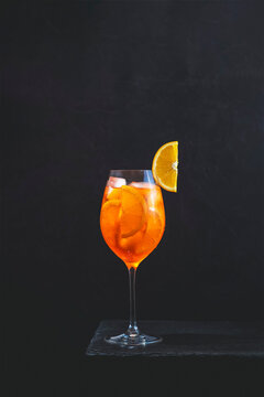 Cocktail aperol spritz in big wine glass with water drops on dark background. Summer alcohol cocktail with orange slices. Italian cocktail aperol spritz on slate board