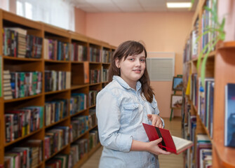 Happy schoolgirl reading a book in the library at school
