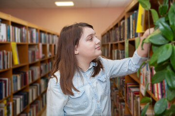 Teen girl taking   book from bookshelves in library, choosing.