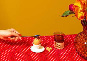 Served breakfast table. Food pop art photography. Tea, egg and flowers on red tablecloth over yellow background. Vintage, retro style interior