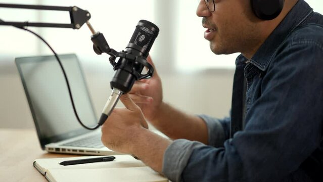 Close-up condenser microphone of content creator man host streaming his a podcast on laptop with headphones interview conversation at home broadcast studio. Male blogger recording voice over radio