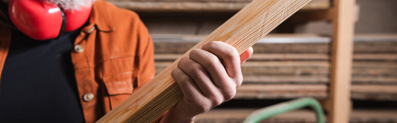 partial view of furniture designer holding plank in carpentry workshop, banner.