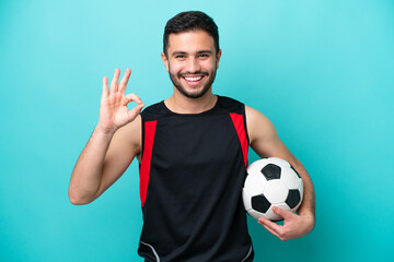 Young football player Brazilian man isolated on blue background showing ok sign with fingers