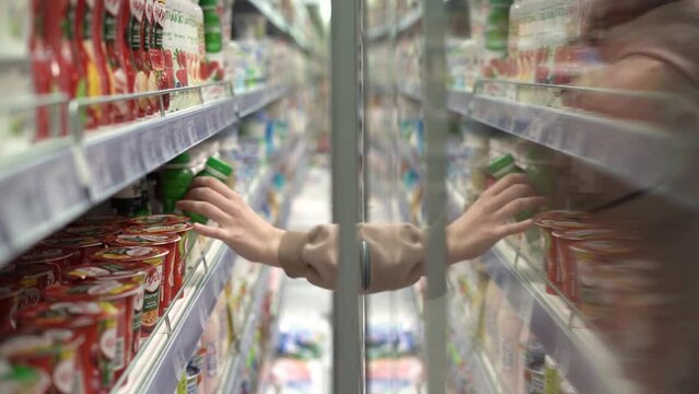 A girl takes a bottle of drink from the refrigerator in the store.