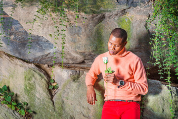 Young African American Man holding white flower, waiting for you at park in New York