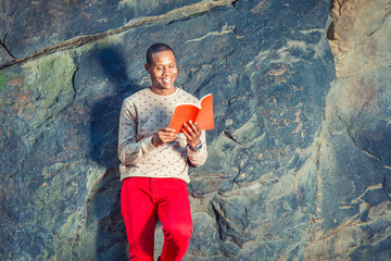 Young African American Man reading red book at park in New York