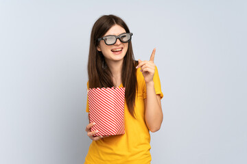 Young Ukrainian girl isolated on white background with 3d glasses and holding a big bucket of popcorns while pointing front