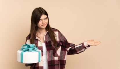 Young Ukrainian girl holding a big cake isolated on beige background extending hands to the side for inviting to come