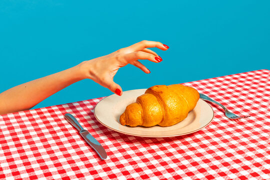 Naklejki Female hand tasting crispy croissant on plaid tablecloth isolated on bright blue background. Vintage, retro style interior. Food pop art photography.