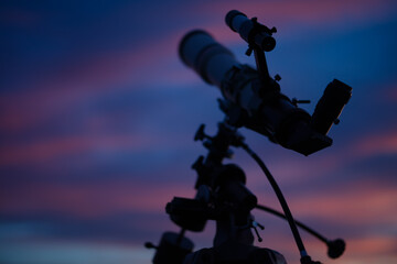 Silhouette of a telescope with colorful skies.