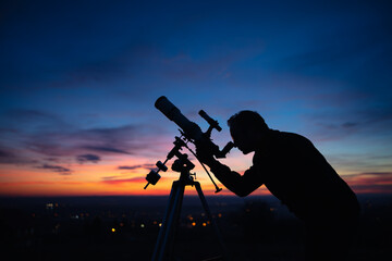 Silhouette of a man, telescope and countryside under the starry