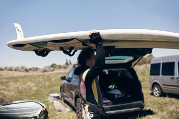 Windsurfer packing and unpacking sports equipment from a car in nature.