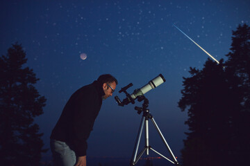 Silhouette of a man, telescope, stars, planets and shooting star under the night sky.