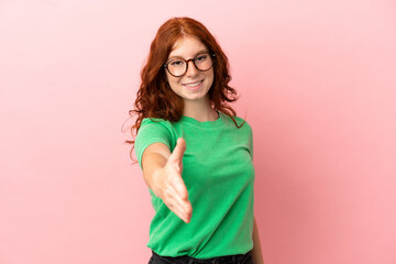 Teenager redhead girl over isolated pink background shaking hands for closing a good deal