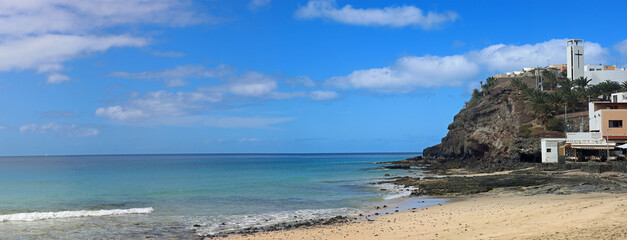 Cliffs at the end of beautiful morro jable beach on fuerteventura island under a blue cloudy sky
