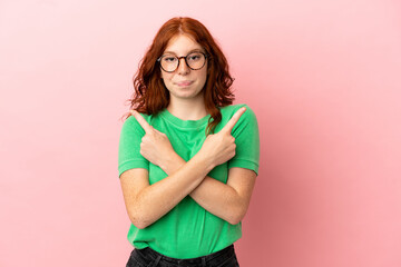 Teenager redhead girl over isolated pink background pointing to the laterals having doubts