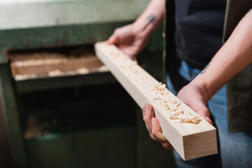 cropped view of woodworker holding board near blurred thickness planner.