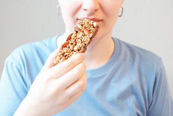 Girl eating protein bar on a gray background close-up.