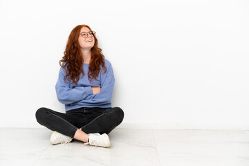 Teenager redhead girl sitting on the floor isolated on white background happy and smiling