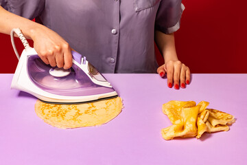 Creative portrait of girl ironing pancakes on lilac color tablecloth. Vintage, retro style...