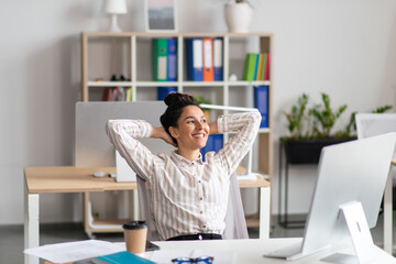 Happy female office worker leaning back on chair, relaxing after successful work at her workplace in office