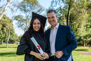 Happy caucasian graduated girl with her father on her graduation day. They are both looking at...