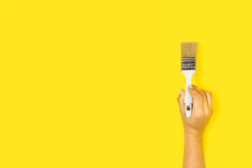 Mano de mujer sosteniendo un pincel brocha sobre un fondo amarillo liso y aislado. Vista de frente y de cerca. Copy space