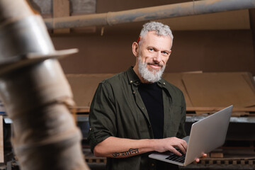 tattooed furniture designer with laptop smiling at camera on blurred foreground.