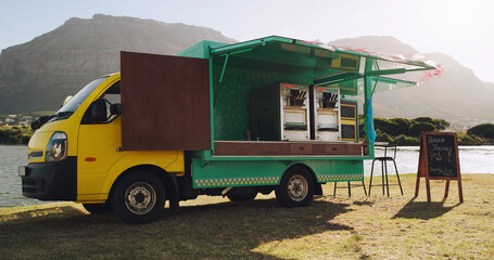 Todays market should bring a lot of clients. Shot of a food truck parked outside next to a lake.