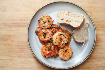 Shrimps in tomato sauce with bread on a plate and a wooden table, copy space, high angle view from above