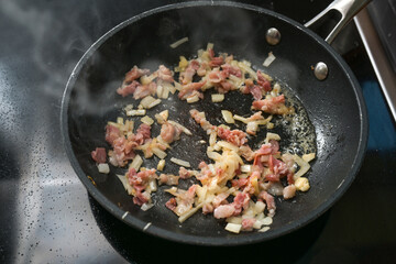 Bacon and onions fry in a hot steaming pan on the stove, cooking at home, copy space, selected focus
