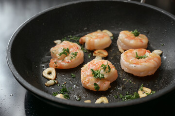 Shrimps fried in a pan with garlic and parsley in olive oil on the stove, cooking a delicious appetizer, copy space, selected focus