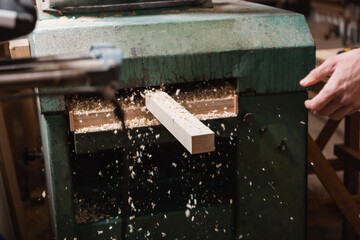 plank and sawdust near thickness planer and cropped carpenter in workshop.