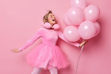 Glad positive woman has festive mood wears dress poses with balloons enjoys special occasion...