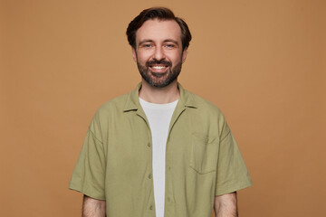 indoor portrait of bearded male posing over beige background looking into camera with bradly smile on his face