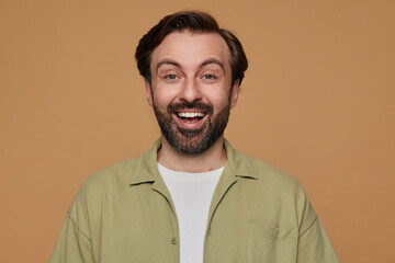 indoor portrait of bearded male posing over beige background looking into camera with bradly smile on his face