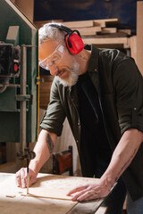 bearded carpenter in goggles cutting plywood with band saw.