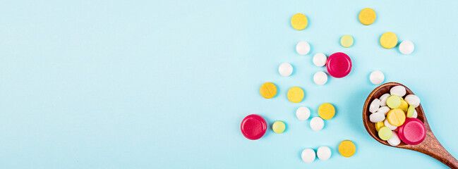 Colorful pills in wooden spoon on a pastel blue background. Flat lay, top view, overhead, mockup, template, copy space. Pharmacy and medical concept