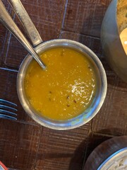 Close up of lentil dahl vegan vegetarian Indian dish with cumin and garlic and spices served in restaurant in metal bowl with spoon on wood table interior for evening restaurant meal