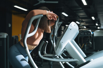 Young tired woman training for cardio equipment at the fitness gym