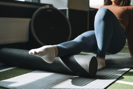Young brunette woman doing stretching pilates on massage roll in fitness club gym