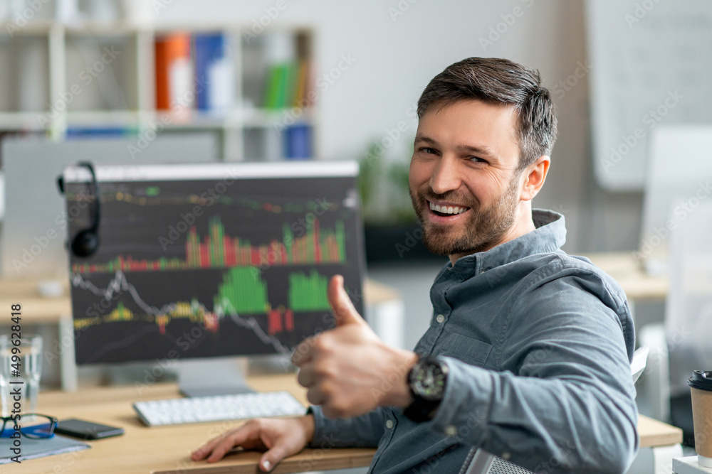 Poster Happy mature businessman working on computer with graphs and charts, sitting in office and showing thumb up