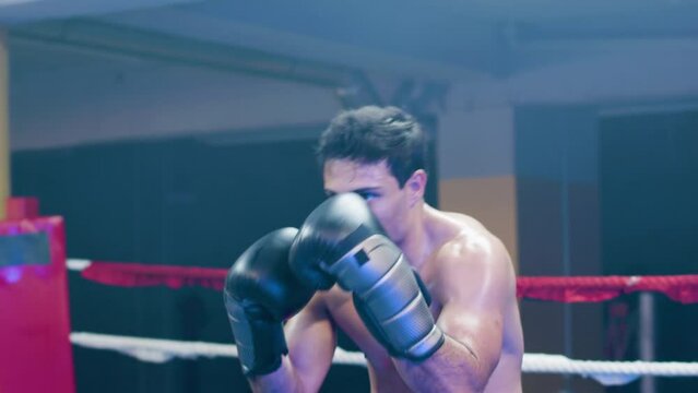 Attractive young man doing shadow fight in boxing ring. Muscular boxer working out indoors, practicing punches and dodging techniques. Handheld shot. Sport, boxing concept