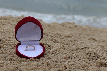 A beautiful ring in a red box in the sand on the beach by the sea. Romantic marriage proposal