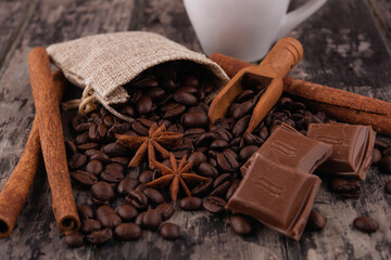cup of coffee with chocolate, cinnamon sticks,   and coffee beans on wooden background