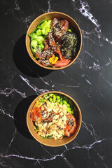 Top view of wok box, bowl of rice on background. Rice fried and stirred with salmon, avocado, onion, cucumber, broccoli, sesame. Chinese, Asian food delivery. Packaging for woks. 