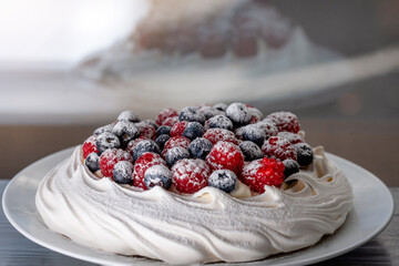 meringue cake with blueberries and raspberries on a plate on green background