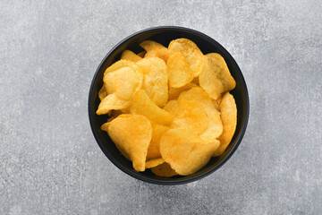 Potato chips. Fast food. Crispy potato chips ceramic black bowl with sour cream sauce and onions in wooden stand on gray kitchen table concrete background. American tradition. Hot BBQ. Top view.